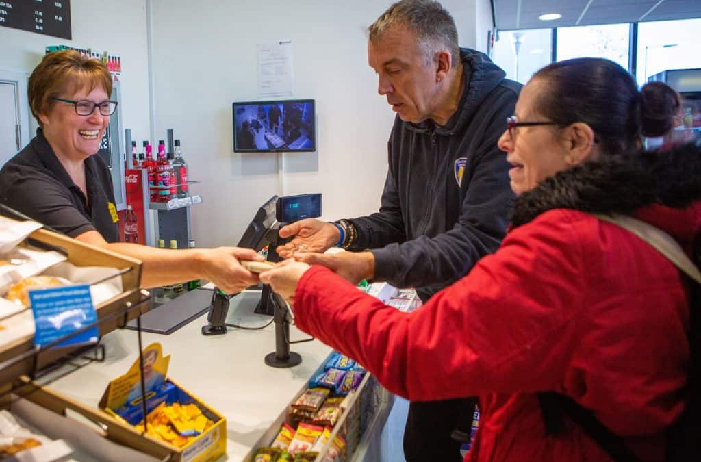 Our Services: Independent Living Services - ILS colleague supporting a client in a shop, paying at a till with a member of shop staff